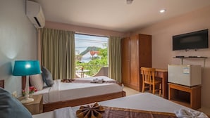 Ett hotellrum med två sängar, ett skrivbord, en tv och en balkong med utsikt över en kulle och byggnader.