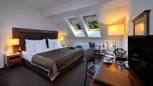 Een hotelkamer met een bed, een bureau met een laptop, een stoel, een televisie en een raam met uitzicht op bomen.