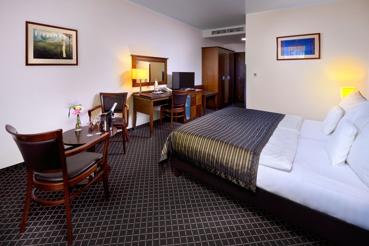 A hotel room with a bed, a desk with a chair, a television, and a mirror.