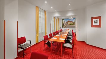 Una sala conferenze con un lungo tavolo, sedie rosse e un tappeto rosso.