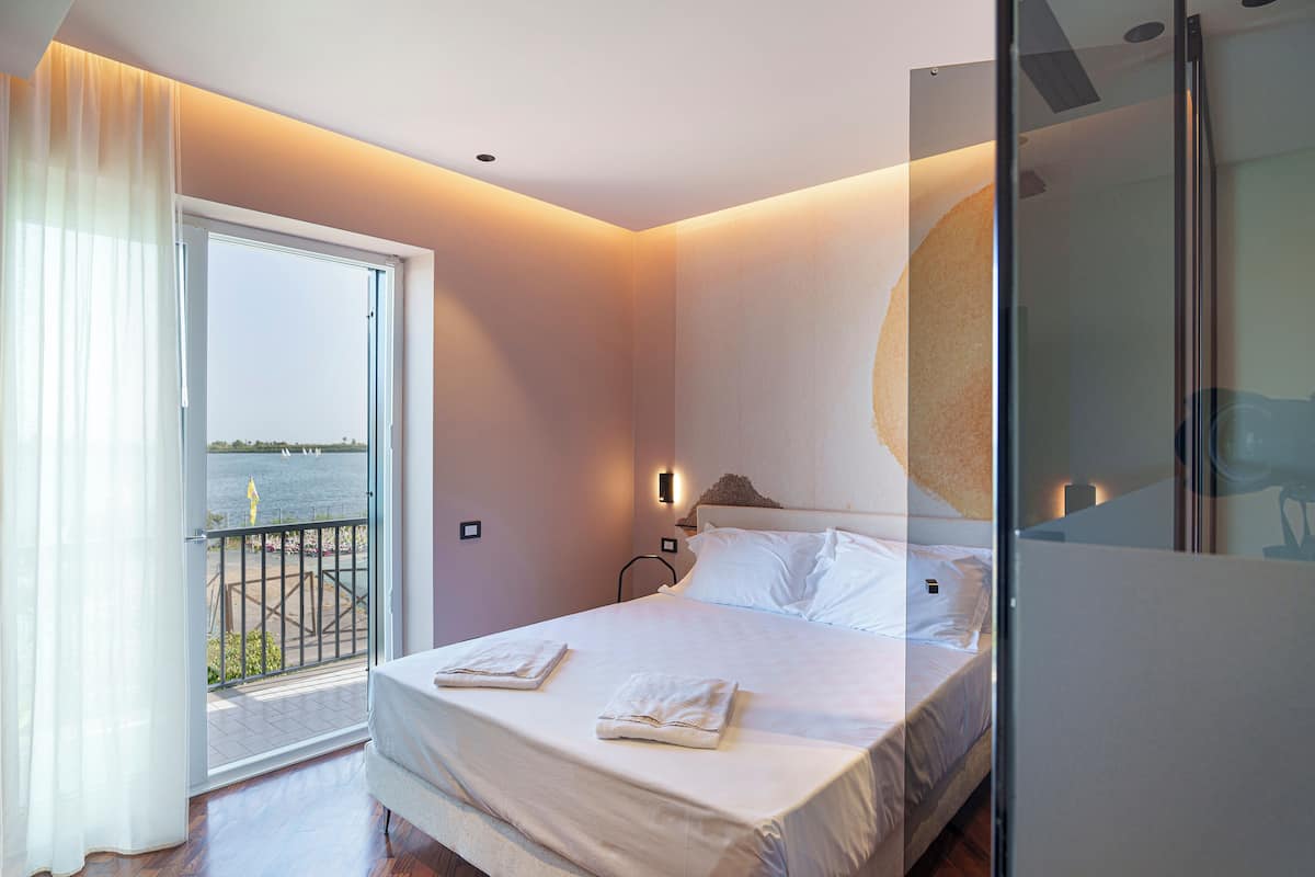 A bedroom with a bed, a nightstand, and a view of the sea through a balcony door.