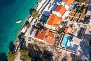 Vista aérea de una zona residencial costera con casas, piscina y un barco en el agua.