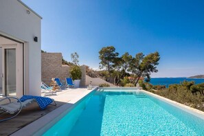 Una piscina con agua cristalina azul, rodeada de sillas de descanso y un muro de piedra.