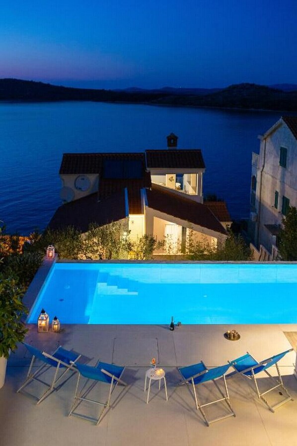 Una villa moderna con piscina, con vista a un cuerpo de agua.