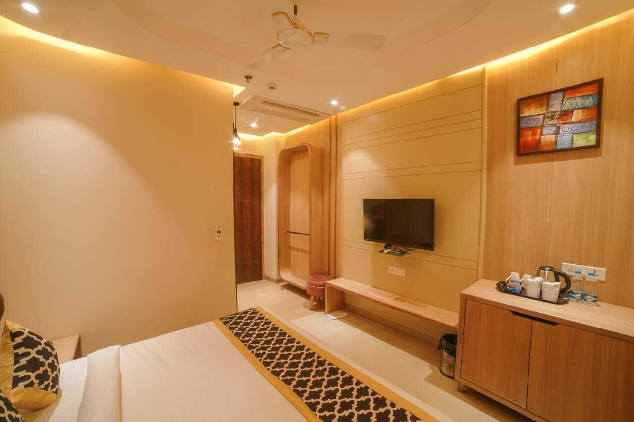 A modern hotel room with a bed, a TV, a wooden cabinet, and a bench.