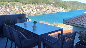 Una terraza con mesa y sillas, con vistas a un pueblo costero y al mar.