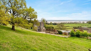 A rural landscape with a stone house, a large tree, and a view of the countryside.