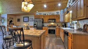 A spacious kitchen with wooden cabinets, granite countertops, stainless steel appliances, and a central island with bar stools. - Pet-friendly, family-sized luxury cabin rental, hot tub, WiFi, firepit (Mineral Bluff)