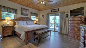 A bedroom with a wooden ceiling, a bed, a bench, a dresser, and a television. - Pet-friendly, family-sized luxury cabin rental, hot tub, WiFi, firepit (Mineral Bluff)