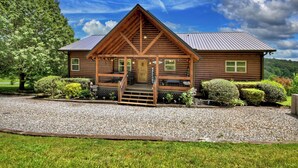 A wooden lodge with a porch, gravel driveway, and well-maintained landscaping. - Pet-friendly, family-sized luxury cabin rental, hot tub, WiFi, firepit (Mineral Bluff)