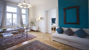 A modern living room with a dining area, a teal accent wall, and a white sofa. - Waterfront Apt w/ River Views & Trendy Location (Praha 5)