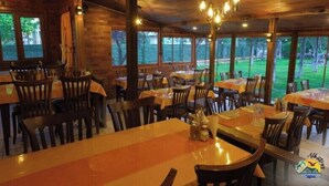 Een restaurant met houten inrichting en grote ramen. Tafels zijn gedekt met stoelen en tafelkleden.