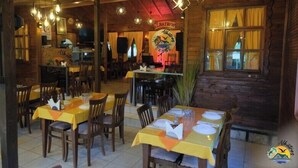 Een restaurant met houten inrichting, tafels gedekt met gele tafelkleden, en een podium met een logo.