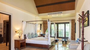 A spacious bedroom with a large bed, a sitting area with a sofa, and a view of greenery through the windows. - Balinese-inspired 3-bedroom villa with private pool, garden, and 5-min walk to Bang Kao Beach (Koh Samui)