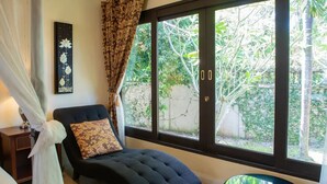 A room with a large window, a dark upholstered chair, a patterned pillow, and a wall-mounted artwork. - Balinese-inspired 3-bedroom villa with private pool, garden, and 5-min walk to Bang Kao Beach (Koh Samui)