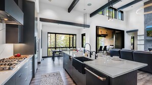 A modern kitchen with a central island, built-in appliances, and a dining area with a view of the outdoors. - Ski Access, Overlooking the Lake + Private Hot Tub & Pets Considered (Whitefish)
