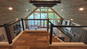 Un ático espacioso con piso de madera, ventanas amplias que ofrecen vistas al exterior y una escalera que conduce a un nivel inferior.