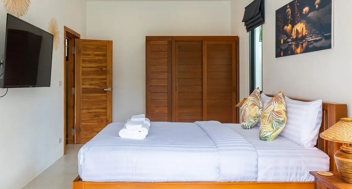 Un dormitorio con cama, televisor, armario y un cuadro en la pared.