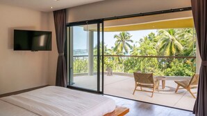 A bedroom with a large bed, a TV mounted on the wall, and a balcony with chairs and a table.