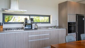 A modern kitchen with a gas stove, microwave, and coffee maker. There is a window above the sink, and a refrigerator to the right.