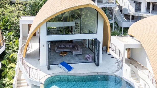 A modern villa with a curved roof, a swimming pool, and a balcony with outdoor seating.