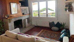 A living room with a fireplace, a sofa, a rug, and a window with a view of greenery. - Intimate Family Villa with big private pool & panoramic sea view (CT)