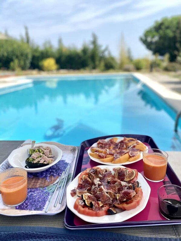 A dining table with plates of food, drinks, and a tray by a pool.