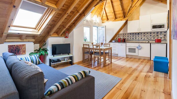 A cozy loft-style living space with a dining area, kitchenette, and a large window providing natural light. - Wooden Top With Terrace (Lisbon)