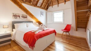 A bedroom with a bed, a red chair, wooden beams, a window, and artwork on the wall. - Wooden Top With Terrace (Lisbon)