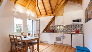 A kitchen with wooden beams, white cabinets, a tiled backsplash, and a dining area with a table and chairs. - Wooden Top With Terrace (Lisbon)