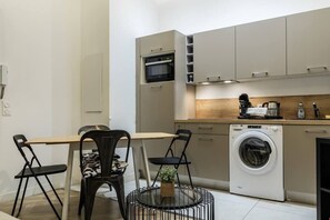A compact kitchen with a microwave, washing machine, and a small dining area with chairs and a table.