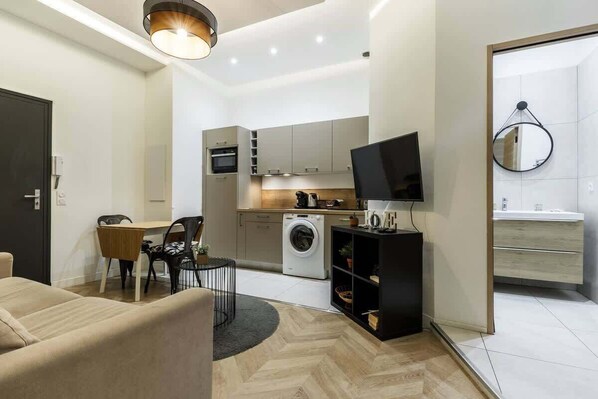 Un espacio habitable compacto con sofá, mesa de comedor, sillas, televisor, lavadora y zona de cocina.