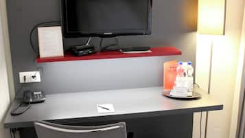 A small workspace with a desk, chair, trash bin, and a flat-screen TV.