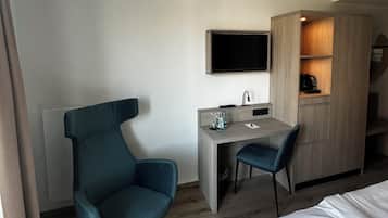 A modern hotel room with a bed, a desk with a chair, a TV mounted on the wall, and a wardrobe.