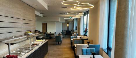 A modern restaurant with a long counter, multiple seating areas, and large windows.