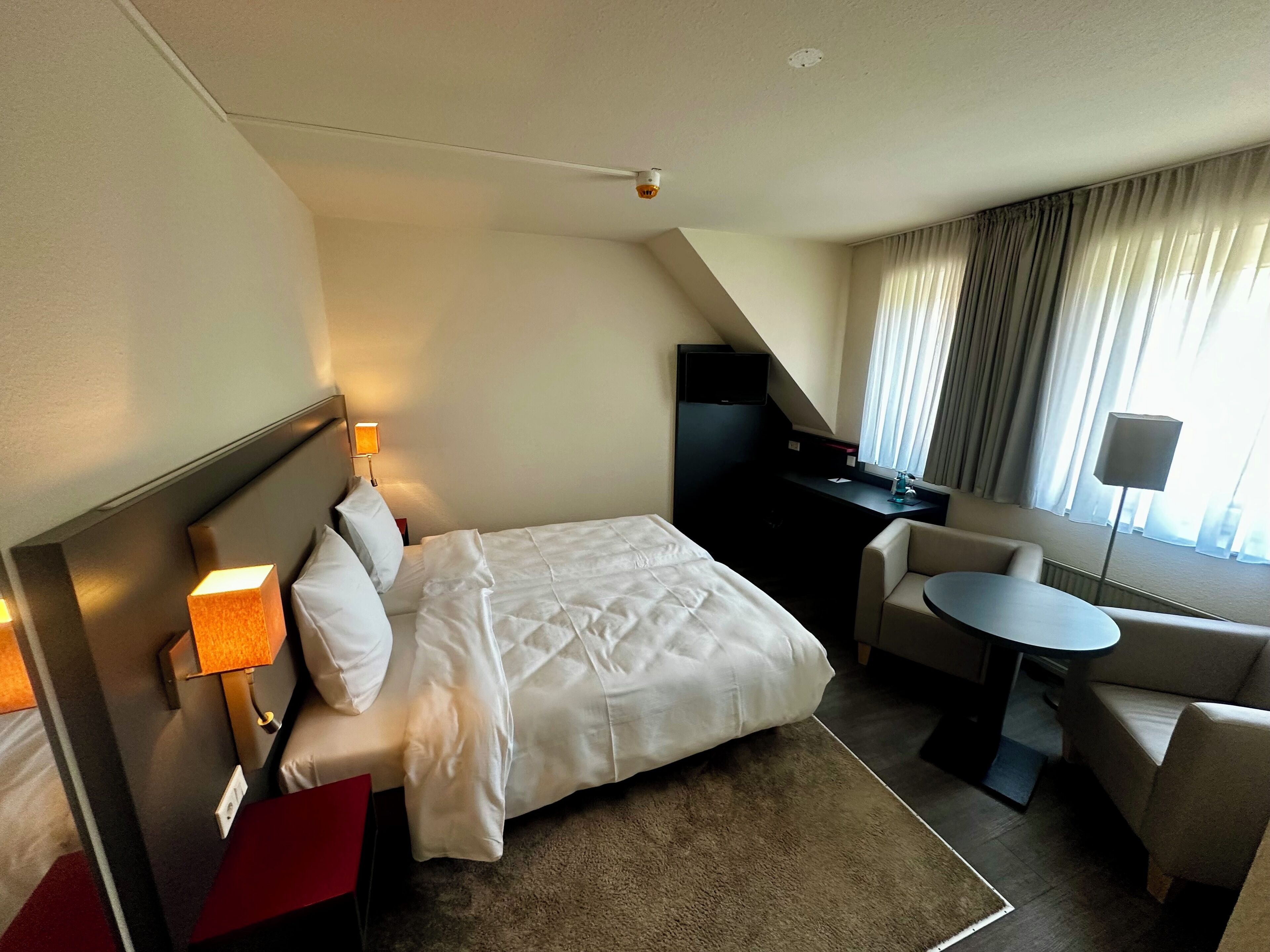 Una habitación de hotel con cama, escritorio, silla y una mesita.