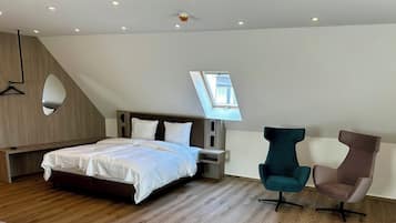 Ein modernes Schlafzimmer mit schrägen Wänden, einem Oberlicht, einem Bett, zwei Stühlen und einer hölzernen Sitzbank.
