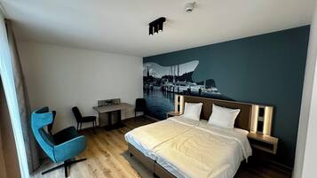 Habitación de hotel con cama, escritorio, dos sillas, un mural en la pared y una lámpara en el techo.