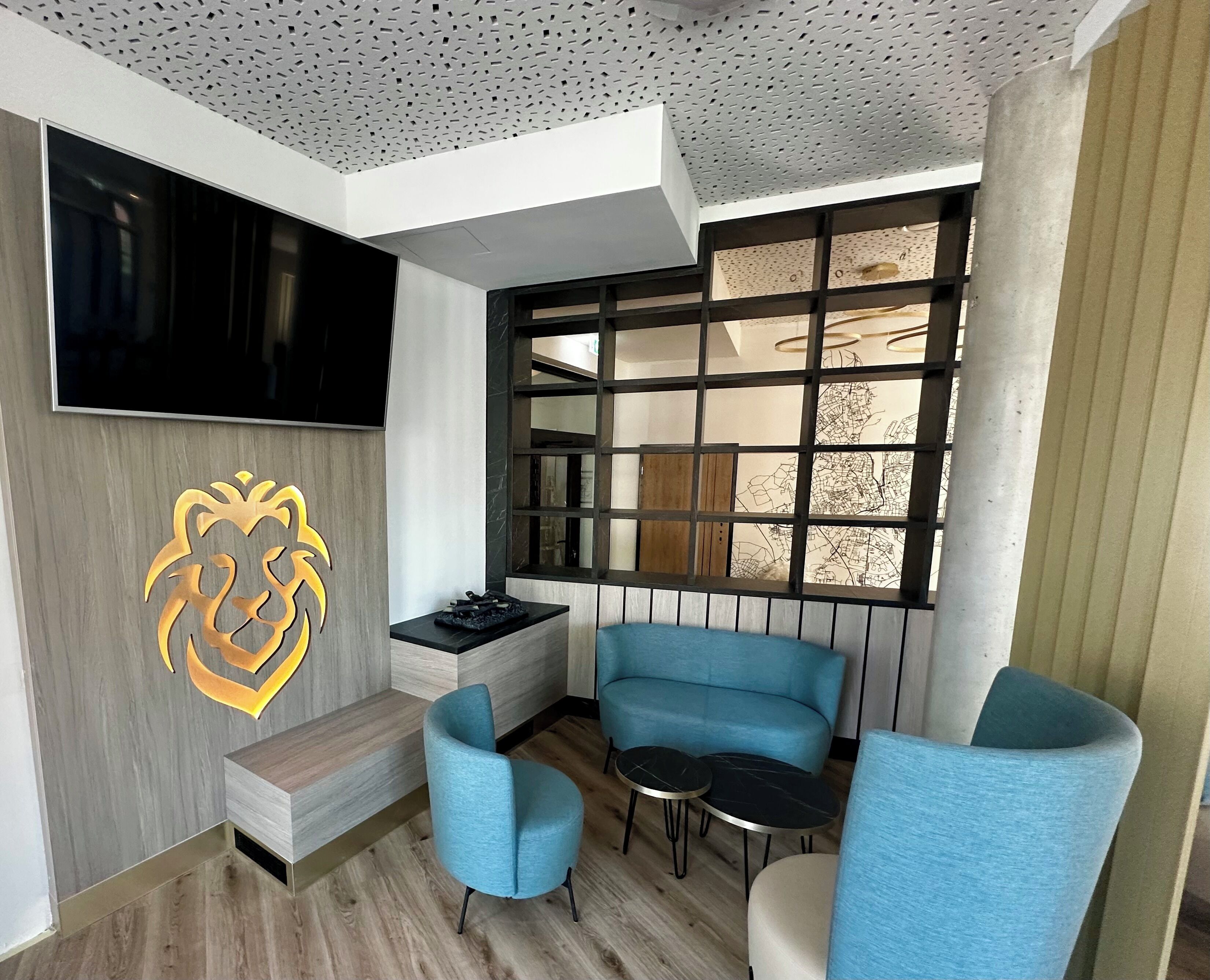 Una sala de estar moderna con televisor, una escultura decorativa de cabeza de león, un sofá azul, una mesita y una ventana con vista a la ciudad.