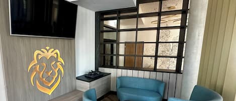 A modern living room with a TV, a decorative lion head, a blue sofa, a small table, and a window with a cityscape view.