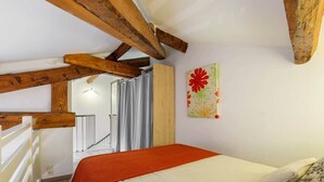 A bedroom with a bed, wooden beams, a window with curtains, and a wall-mounted artwork. - Nice duplex with patio (Niza)
