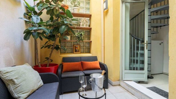 A cozy outdoor seating area with a sofa, cushions, a table with glasses and a champagne bucket, a potted plant, and a staircase. - Nice duplex with patio (Niza)