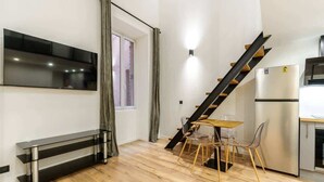 A modern kitchen with a built-in stove, a dining area with a table and chairs, a staircase, and a flat-screen TV mounted on the wall.