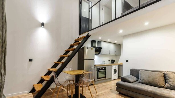 A modern interior with a staircase, a dining area, a sofa, and a kitchen.