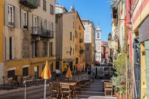 A narrow street with outdoor seating, buildings with balconies, and a white van parked on the side.
