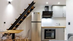 A compact kitchen with a refrigerator, oven, microwave, and a wooden dining table with chairs.