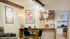 Un salon moderne comprenant un canapé, des fauteuils, une table basse et un coin repas avec une table et des chaises. On y trouve également des étagères remplies de livres et des tableaux encadrés accrochés au mur.