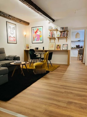 Ein modernes Wohnzimmer mit einer Couch, Sesseln, einem Couchtisch und einem Essbereich mit Tisch und StĂŒhlen. An den WĂ€nden befinden sich BĂŒcherregale mit BĂŒchern und gerahmte Bilder.