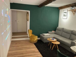 Ein Wohnzimmer mit einer Couch, einem gelben Sessel, einem Couchtisch und einer Projektionsleinwand, auf der ein Film lÀuft.