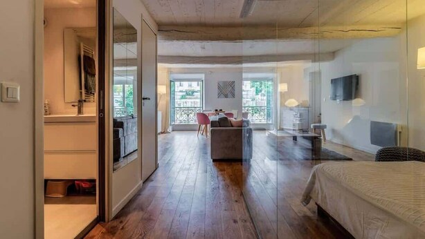 Habitación de hotel con piso de madera, una cama, un televisor y un separador de vidrio.